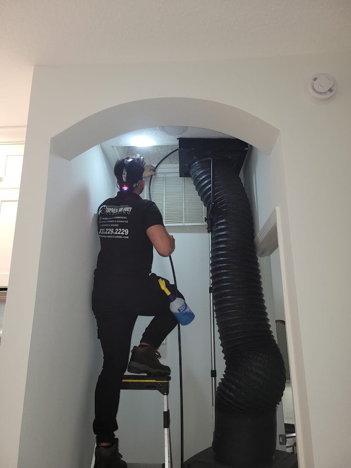 Express Air Duct Cleaning technician on a step ladder cleaning a ceiling air return with a black flexible hose